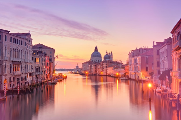 Romantisch Venetië bij zonsopgang, zonsopgang. Stadsbeeld van Canal Grande in Venetië, met Santa Maria della Salute Basilica weerspiegeld in kalme zee. Straatverlichting weerspiegeld in kalm water.