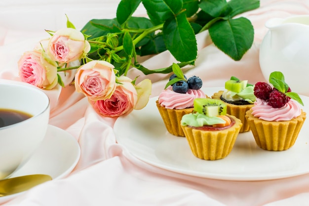 Romantische compositie voor Valentijnsdag, vakantie, verjaardag. mini-taartjes met room en fruit op een bord, een kopje koffie, een boeket rozen.