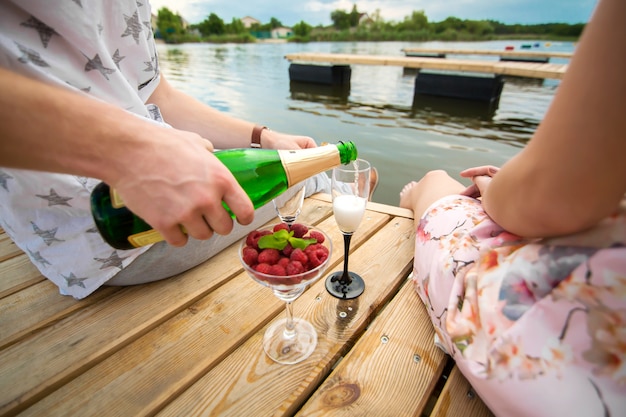 Romantische date verrassing. Een jonge man en een meisje op een houten pier. De man giet champagne in de glazen.