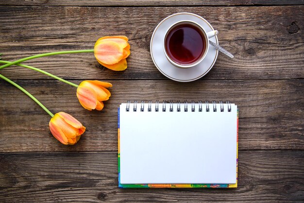 Romantische feestelijke foto met mooie roze en oranje tulpen, een kopje thee, een notitieboekje op een houten rustieke achtergrond