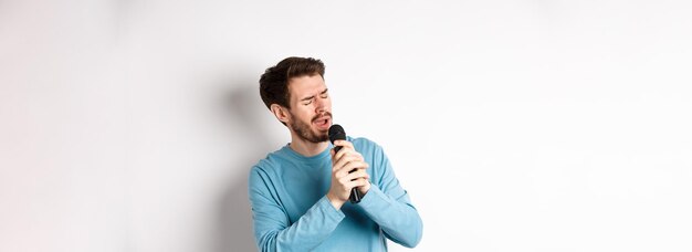 Romantische man die een lied zingt in de microfoon bij karaoke die op een witte achtergrond staat