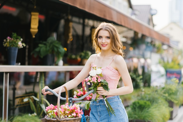 romantische meisje staat en houdt een fiets met een mand met bloemen op een zonnige zomer