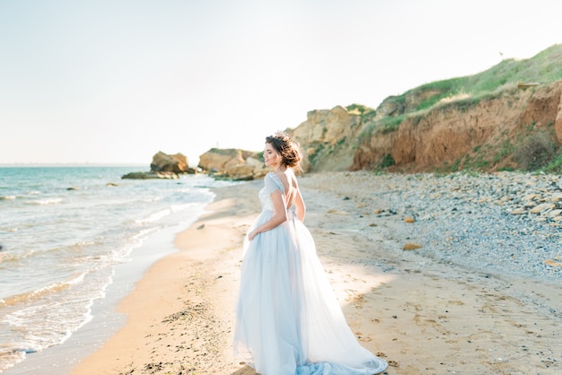 Romantische mooie bruid in luxe lichte chiffon jurk poseren in de buurt van de zee