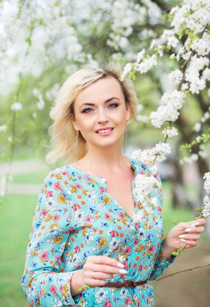 Romantische mooie vrouw in een park op het meer staat tegen een bloeiende boom. mooie vrouw in een gebloemde jurk