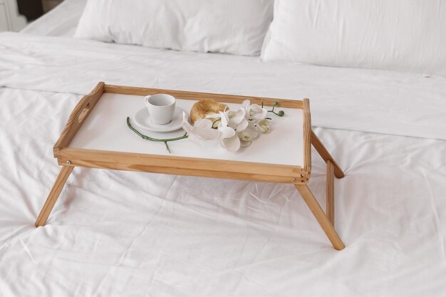 Romantische ochtend. Houten salontafel met bloemen op bed met plaid, koffiekopje, bloemen en donut.