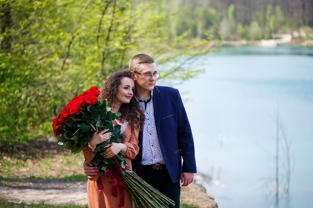 Romantische ontmoeting van jongeren. Een jonge vrouw stemde ermee in om met haar man te trouwen. Een man in een pak met een boeket rode rozen geeft het meisje een boeket en ze kussen in het bos