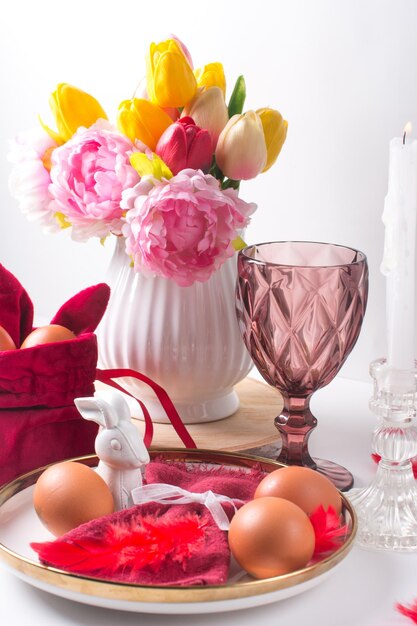 Romantische paastafel met kaarsen wit bord roze wijnglas Tafeldecoratie met konijn en beschilderde eieren in rode en witte kleuren