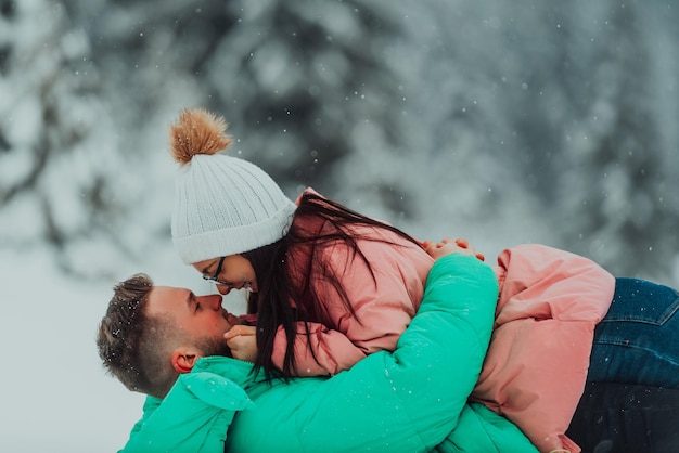 Romantische vrouw en man tijdens de winterdatum met sneeuwvlokken buiten. Het gelukkige paar ging liggen en kuste elkaar in de sneeuw. Hoogwaardige foto