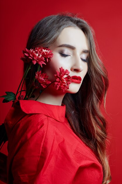 Romantische vrouw met lang blond haar en bloemen in haar handen in een rode jurk, gladde schone huid