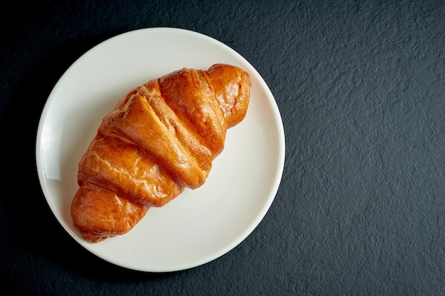 Romige zoete croissant in witte plaat op zwarte achtergrond