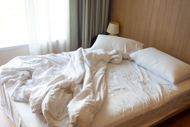 Foto rommelig bed. paarkussens met witte deken op onopgemaakt bed.