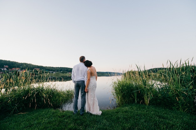 Romnatic portrait from behind of wedding couple looking at big lake at sunset.