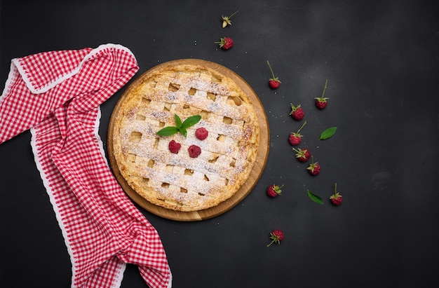 Rond gebakken taart met appels en bestrooid met poedersuiker op een zwarte tafel