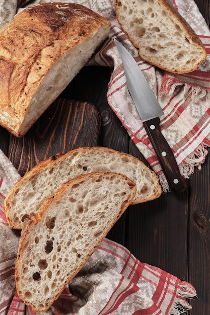 Rond rustiek brood zonder kneden in stukjes gesneden op een snijplank op een oude donkere rustieke tafel Zelfgemaakte volkoren broodlay-out op het verticale tafelframe