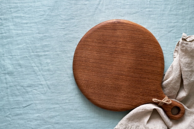 Ronde houten snijplank op blauw linnen textiel tafelkleed