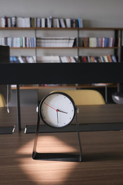 Ronde klok op tafel tegen de achtergrond van een bibliotheek