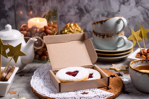 Ronde koekjes met hartvormige jam in een geschenkdoos onder kerstversiering en kaarsen op een grijze tafel