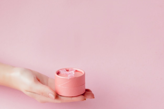 Ronde roze geschenkdoos in de handen van vrouwen op een roze copyspace