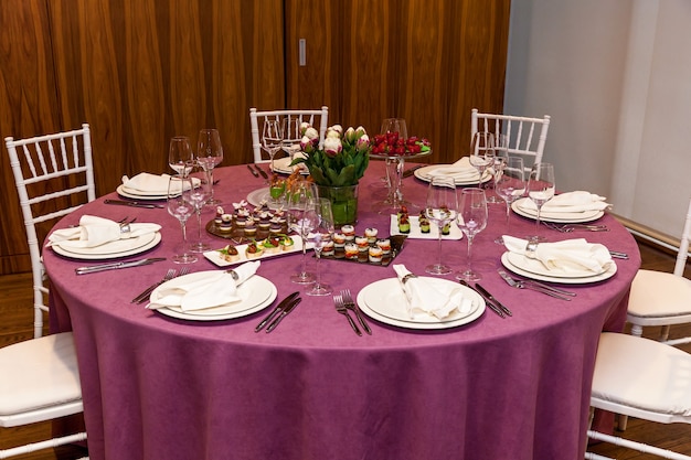 Ronde tafel met roze tafelkleed en bestekset met hapjes voor het banket. Horeca,
