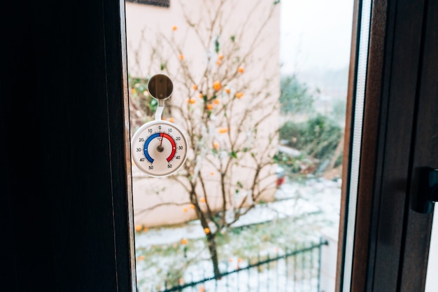 Ronde thermometer op het raam. 5 graden Celsius. De sneeuw buiten het raam.