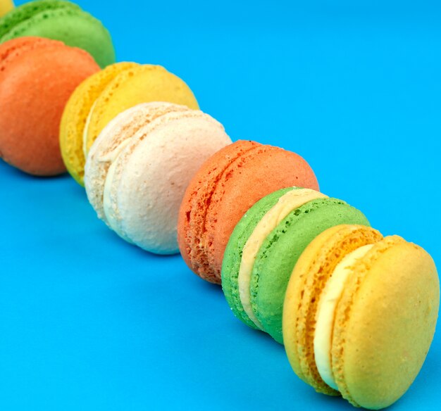 Ronde veelkleurige gebakken macarons met room liggen in een lijn op een blauw vlak