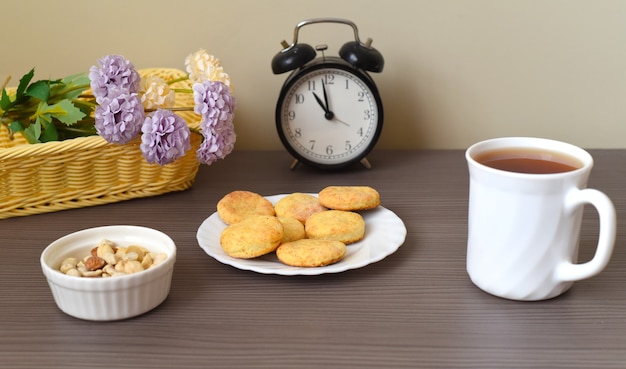 Ronde zelfgemaakte koekjes op een bord naast kopje thee en wekker