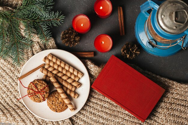 Rood boek, koekjes op een bord en kaarsen op een gebreide deken.