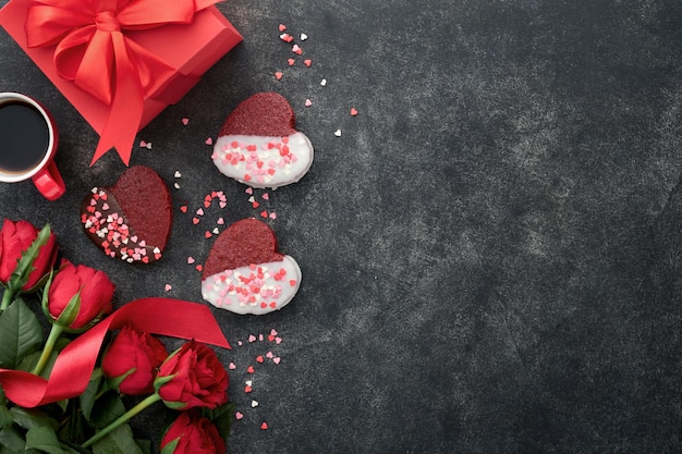 Rood fluweel of brownie koekjes op hartvormig in chocoladesuikerglazuur met rode rozen en geschenkdoos op zwarte achtergrond Dessertidee voor Valentijnsdag Moeders of Vrouwendag Dessert voor Valentijnsdag