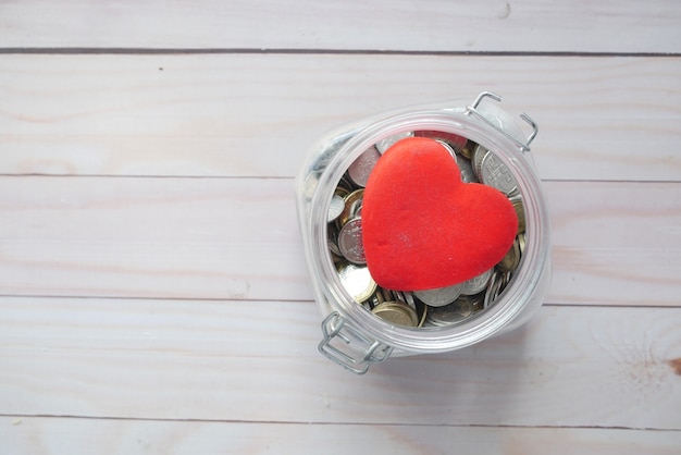 Rood hart en munten in een pot op houten achtergrond