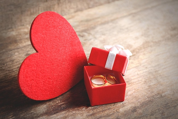Rood hart en trouwringen in een doos op houten close-up als achtergrond