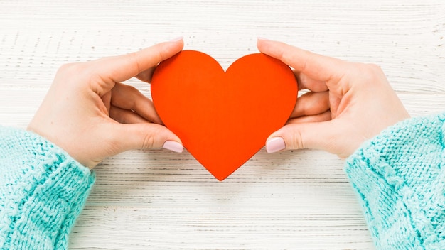 Rood hart in de handen van een meisje in een trui close-up op een houten witte achtergrond