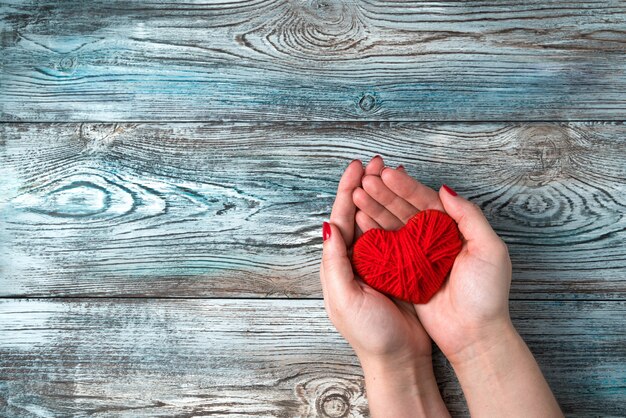 Foto rood hart in de handen van een vrouw op een grijsblauwe houten achtergrond.