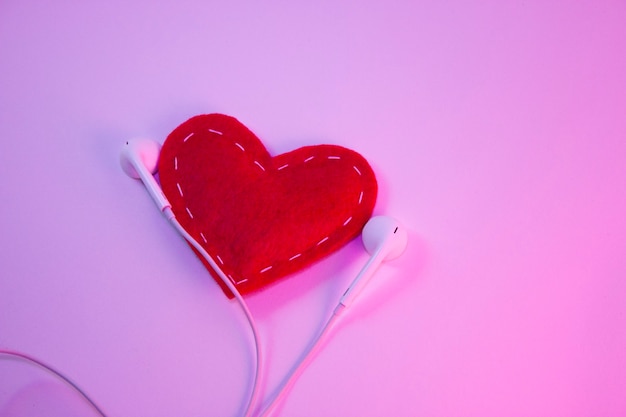 Rood hart stof met witte draden en witte koptelefoon op een witte achtergrond met roze licht. Muziekconcept, favoriete muziek