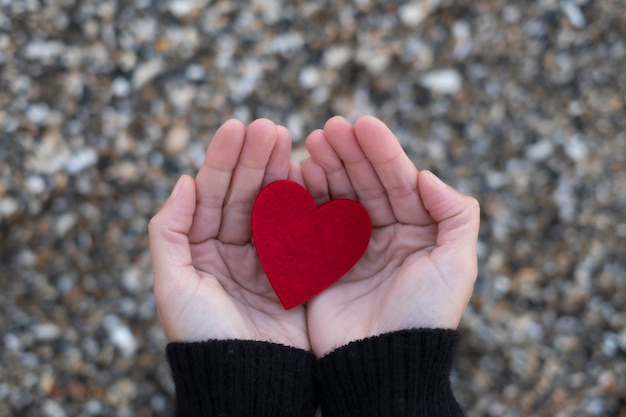 Rood hart tussen de handen van een vrouw op strandstenen. Concept San-valentijnskaart