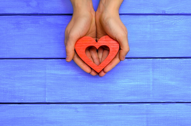 Rood houten hart in handen op een blauwe houten achtergrond.