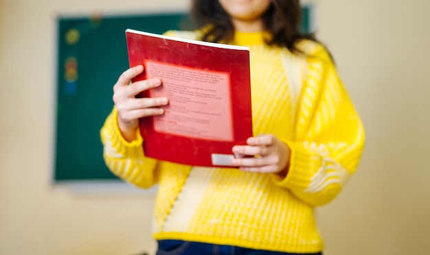 Rood leerboek in handen op vooraanzicht. Meisje in gele trui op onscherpe achtergrond.
