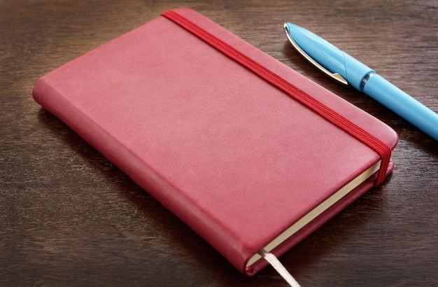 Rood leernotitieboekje met pennen op houten lijst.