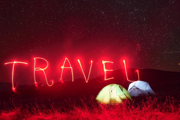 Rood neon reiswoord twee verlichte tenten onder de sterren in de bergen 's nachts