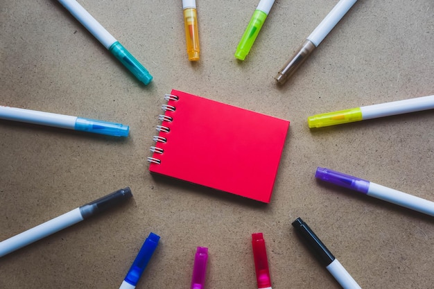 Rood notitieblok voor notities met rode bladen Lege ruimte voor notities Mocap Op warme okerkleurige kraftachtergrond Klein notitieboekje met veermechanisme rustend op tafel omgeven door stiften Creativiteitsschool voor kinderen