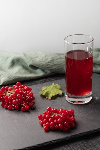 Rood sap van viburnum in een glas op een lichttafel. In de buurt van viburnumbessen en linnen doek. Gezond eten. Ruimte kopiëren