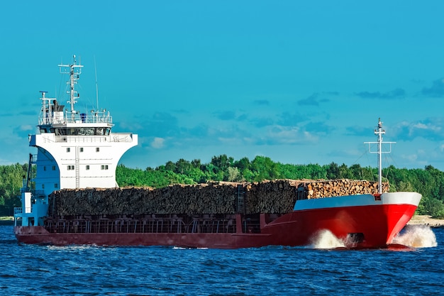 Rood vrachtschip volledig geladen met hout dat op heldere dag beweegt