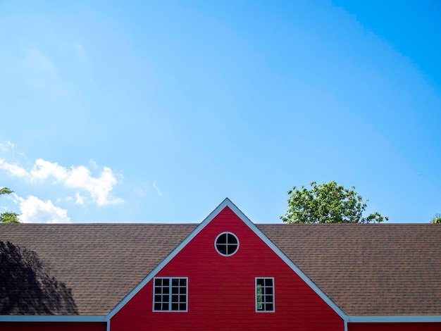 Rood zadeldak van groot huis bedekt met wit houten frame en versierd met rond en vierkant raam op blauwe hemelachtergrond met kopie spacexA