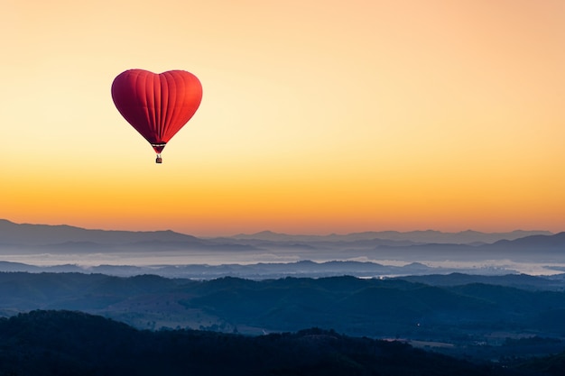 Roodgloeiende luchtballon in de vorm van een hart dat over de berg vliegt