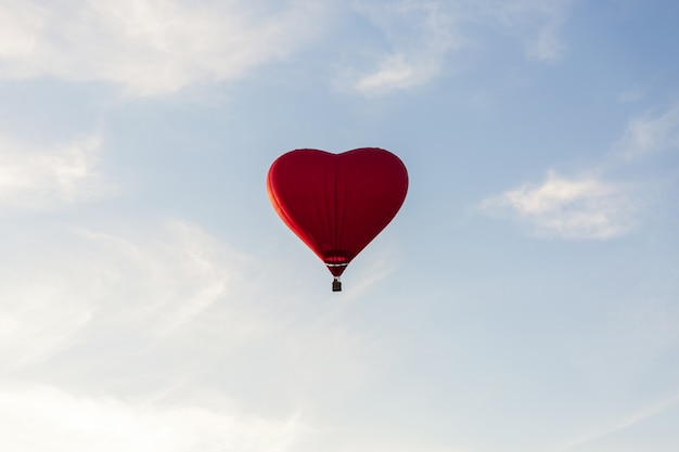 Roodgloeiende luchtballon in de vorm van een hartvlieg in hemel. Liefde, huwelijksreis en romantisch reisconcept