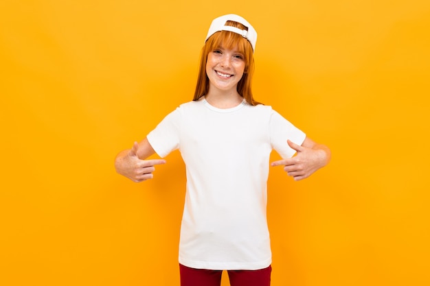 Roodharig charmant meisje in een wit t-shirt op een van een oranje muur, wijst haar vingers naar zichzelf, model