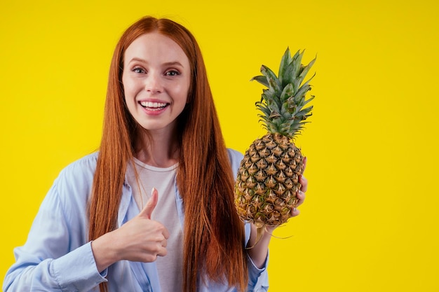 Roodharig gembermeisje met ananas op studio gele achtergrond.