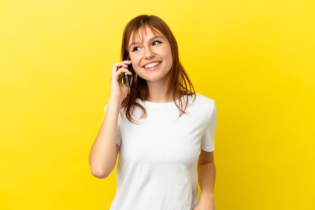 Roodharig meisje dat op gele achtergrond een gesprek met de mobiele telefoon met iemand houdt