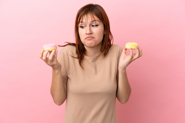 Roodharig meisje geïsoleerd op roze achtergrond met donuts