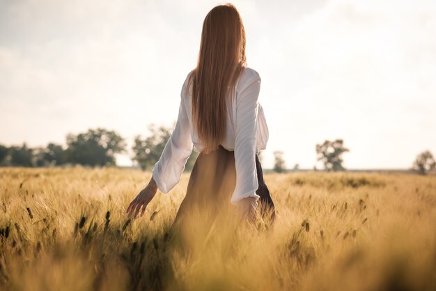 Roodharig meisje in een tarweveld bij zonsondergang. mooie vrouw in gouden veld bij zonsondergang, achtergrondverlichting warme tinten