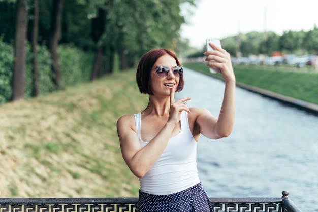 Roodharig meisje lacht in zonnebril praten op videochat via smartphone wandelen in het park.
